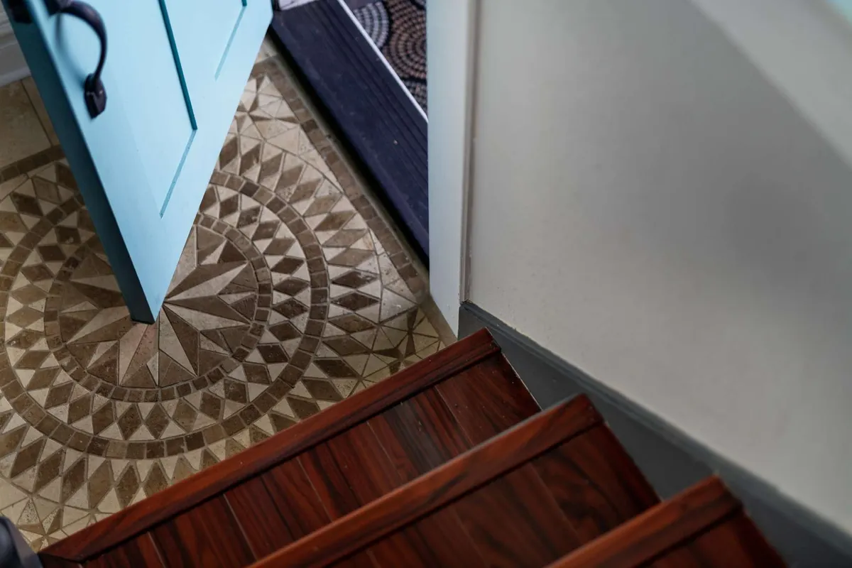 This image presents a blue front door framed by decorative tile flooring and a wooden staircase visible just beyond the threshold. The scene captures the inviting entrance to the home, suggesting a welcoming transition from outdoor adventures back into the comfort of the residence.