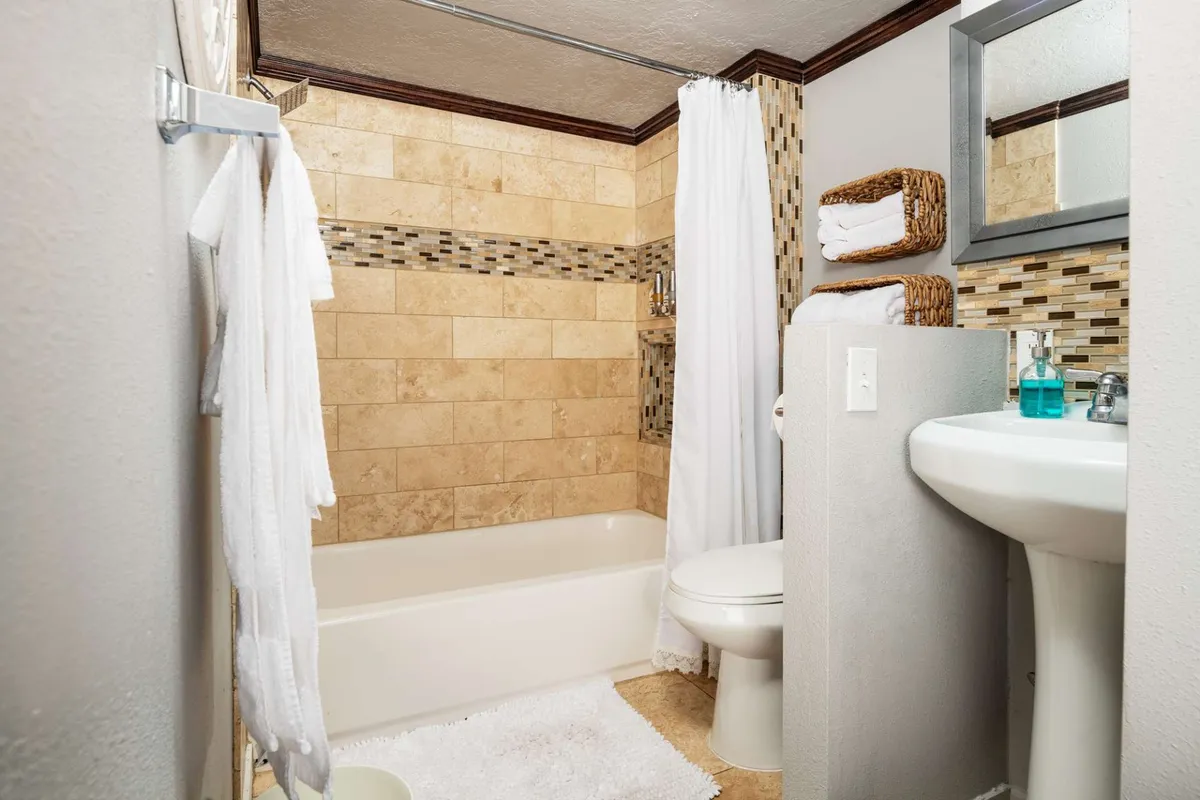 A modern, spa-inspired bathroom with a bathtub, sink, towels, and decorative wall tiles. The space feels fresh, clean, and calming, ideal for unwinding after a long day or starting the morning refreshed.