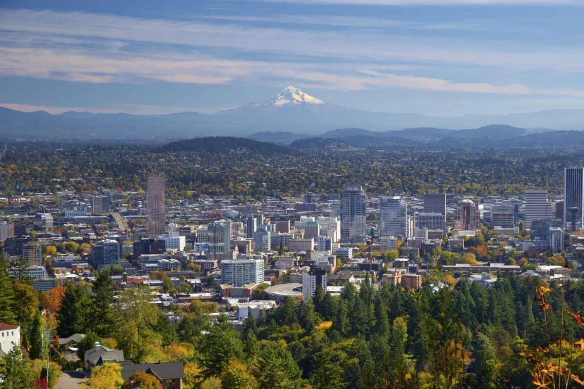 A breathtaking view of Mount Hood with the city skyline and lush trees in the foreground, captured at sunset. The vista highlights opportunities for nearby nature outings and sightseeing.
