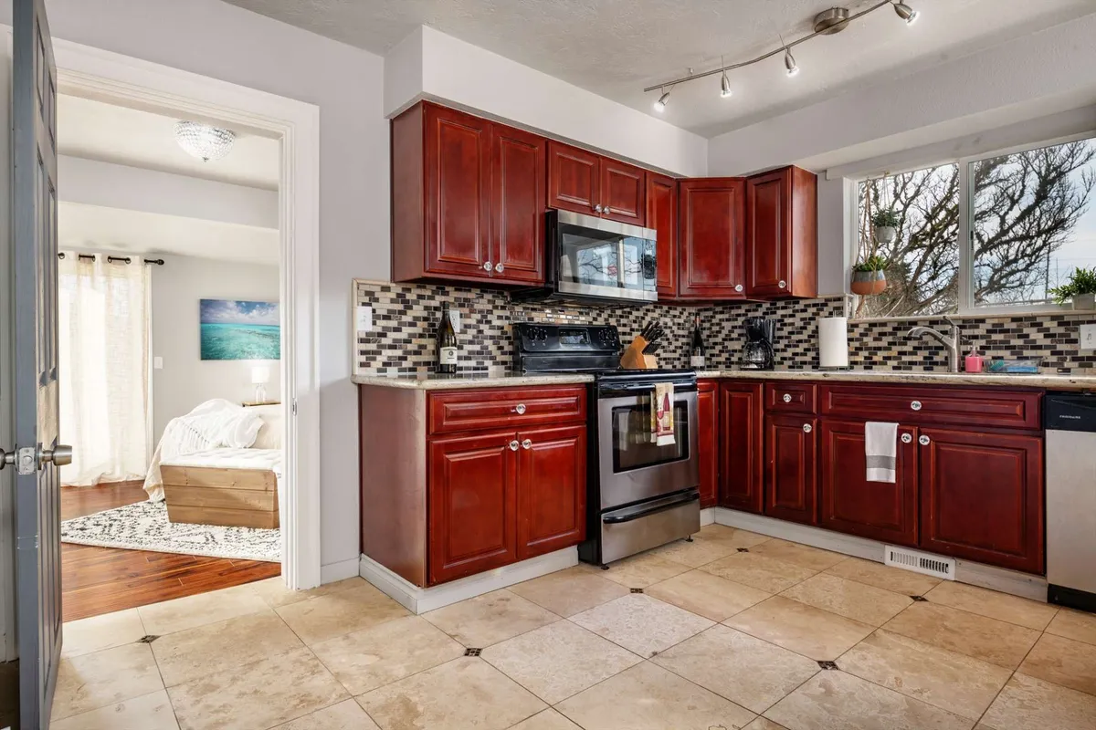A warm, welcoming kitchen featuring striking red cabinetry, modern appliances, a tile backsplash, and a kitchen window that brings in natural light. The area is clearly designed for cooking and entertaining, with space for gatherings and culinary activity.