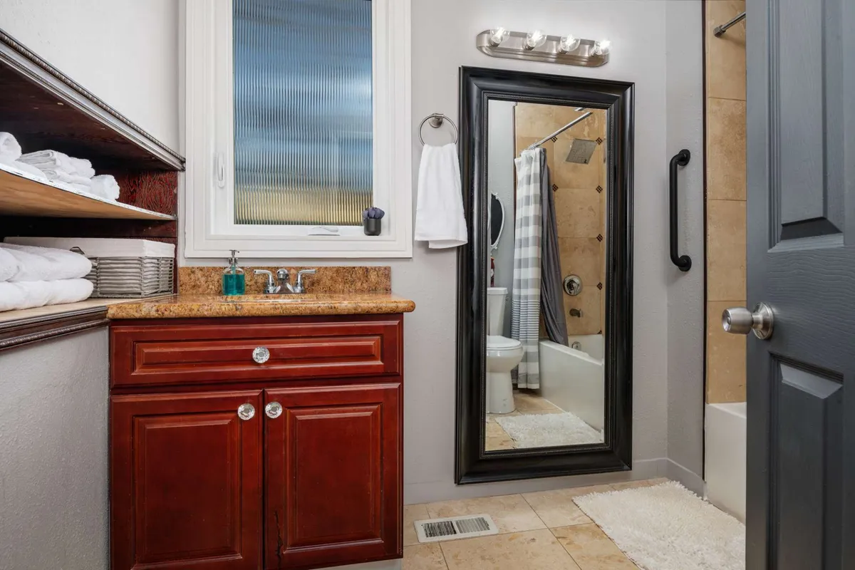 A modern en-suite bathroom featuring a sleek vanity with sink, a large mirror for daily routines, a spacious shower area, and textured wall tiles that add to the tranquil ambiance. The space is designed for relaxation and ease, with natural tones and elegant fixtures.