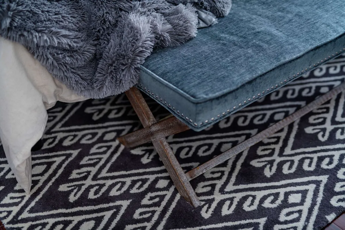 A cozy lounge area featuring a plush grey throw blanket, textured blue cushion, and an intricate patterned rug. The inviting ambiance encourages relaxing, socializing, and quiet moments, ideal after a day spent exploring with pets.