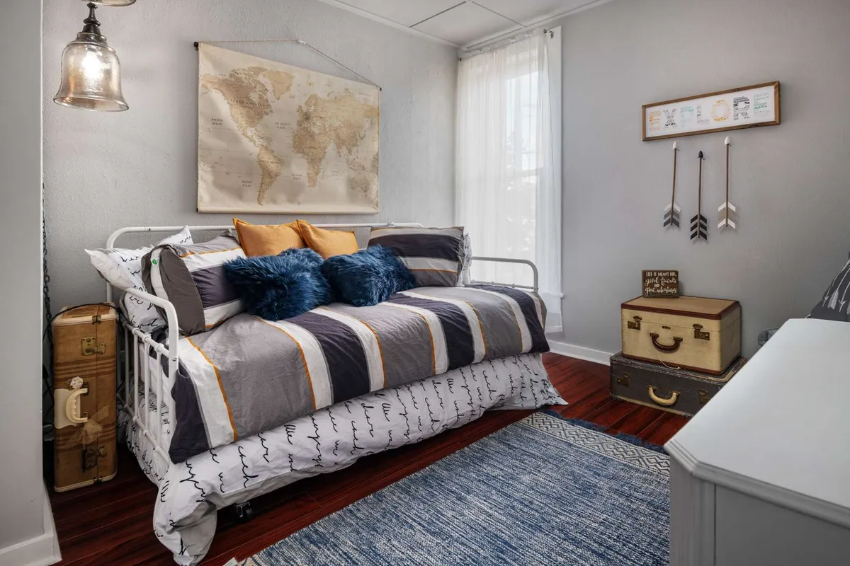 A playful, travel-themed space with a daybed adorned with colorful pillows, a world map on the wall, vintage suitcases, decorative arrows, and a blue area rug. The area invites exploration and cozy gatherings.