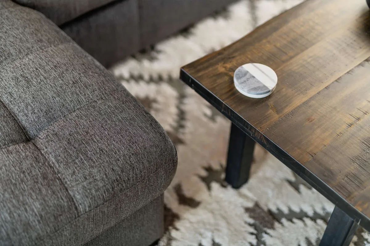 A light-filled living space featuring a gray sofa, wooden coffee table, and decorative coaster. The atmosphere is open and inviting, suggesting a perfect spot for relaxing or gathering with loved ones.