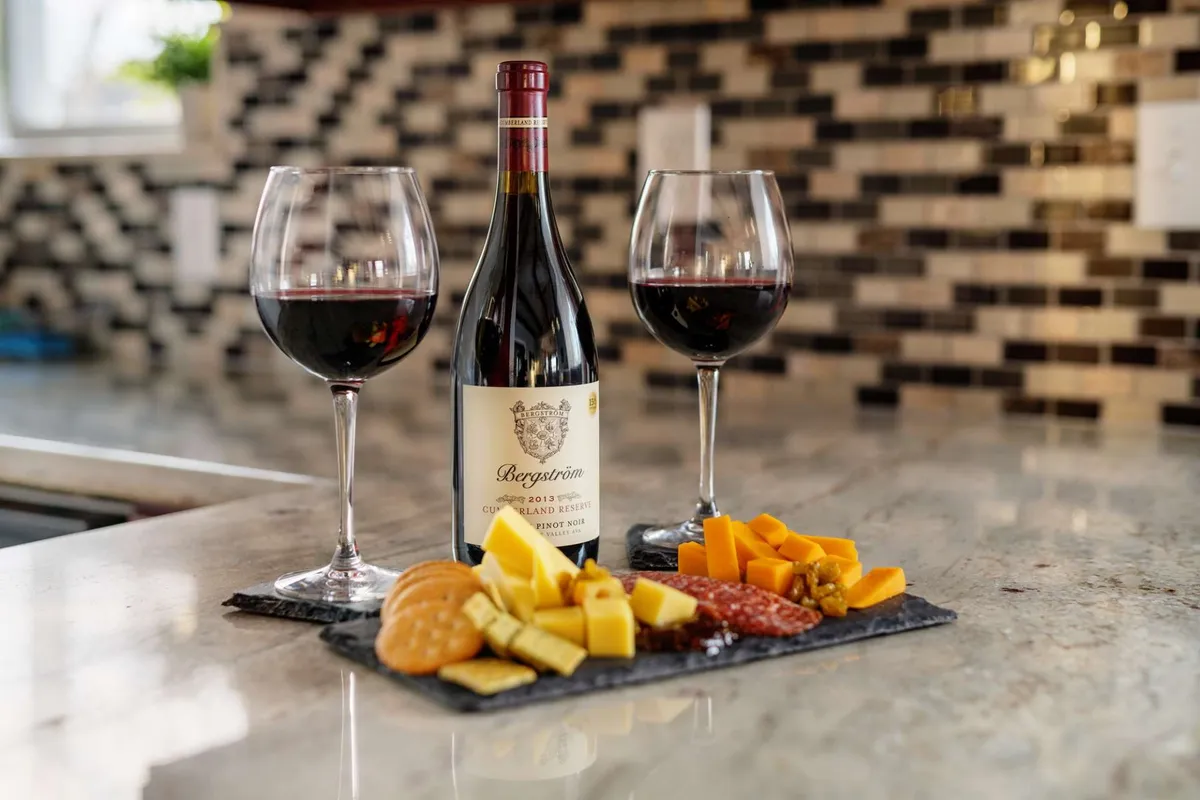 The image spotlights a bottle of wine with two filled glasses and a cheese and charcuterie platter arranged on a wooden table. The cozy scene is set for an intimate tasting experience, echoing the local winery excursions highlighted in the section.