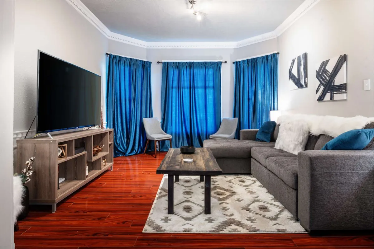 A comfortable living room featuring a plush sofa, coffee table, television, and soft curtains. The space is arranged for socializing, relaxing, and cozy movie nights, with modern décor that feels inviting and warm.